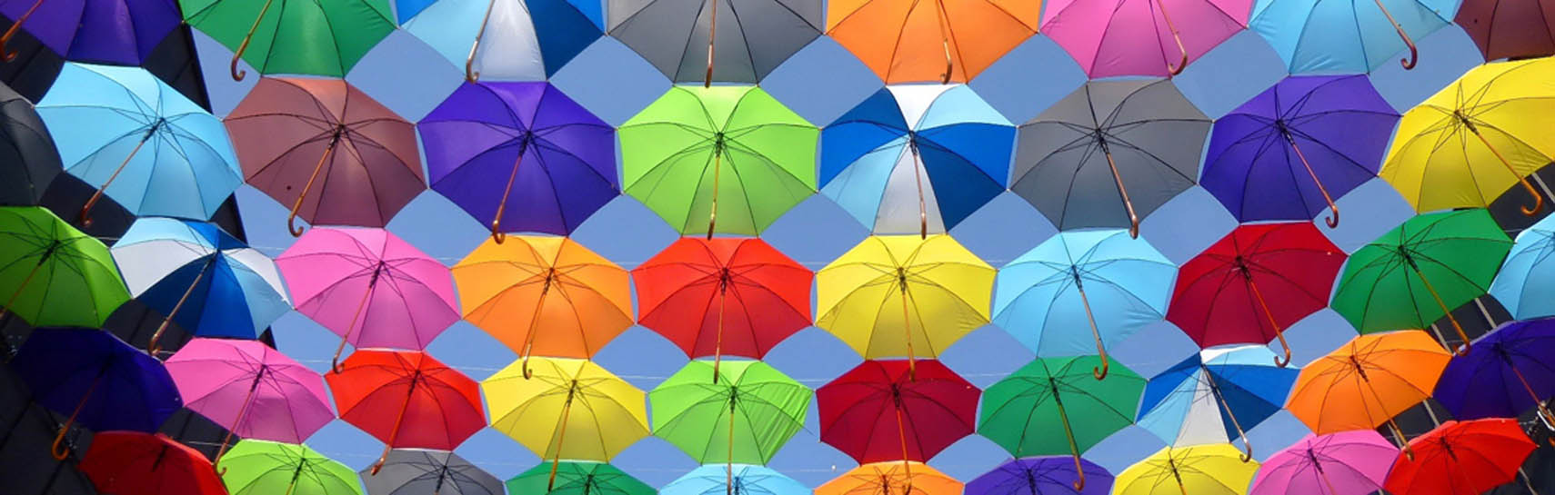 Hunderte bunte Regenschirme liegen auf Leinen, die zwischen Häusern gespannt sind